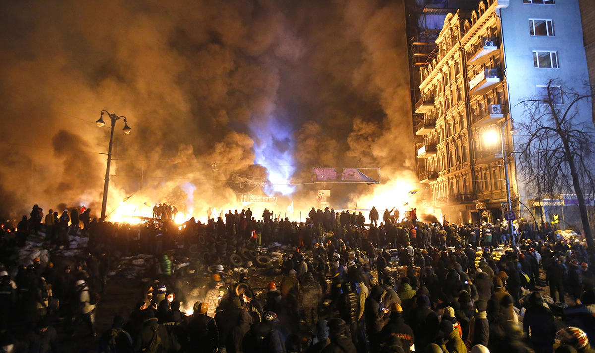 FILE - In this file photo taken on Saturday, Jan. 25, 2014, smoke and fireballs rise during clashes between protesters and police in central Kiev, Ukraine. The "Heavenly Hundred" is what Ukrainians in Kiev call those who died during months of anti-government protests in 2013-14. The grisliest day was a year ago Friday _ Feb. 20, 2014 _ when sniper fire tore through crowds on the capital's main square, killing more than 50 people. A year later, so much has changed. Russia has annexed Ukraine’s Crimean Peninsula, Ukraine has a new president and government, and the country is embroiled in a war in the east with Russia-backed separatists that has killed over 5,600 people and forced a million to flee. (AP Photo/Sergei Grits, File)